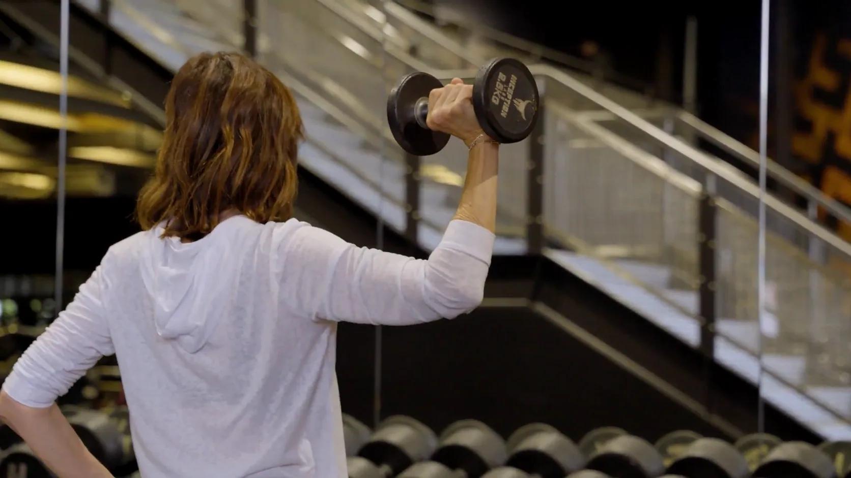 Woman training with an Inception dumbbell on the free weights floor at Inception Gym Christchurch, beside a full dumbbell rack