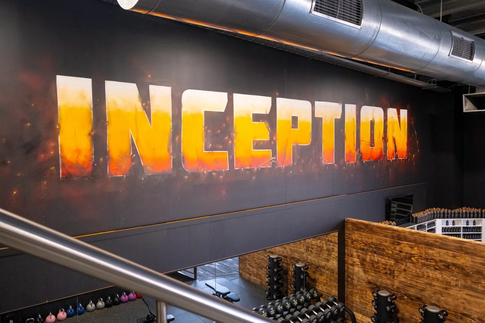 Large flame-styled INCEPTION mural on the training floor wall at Inception Gym Christchurch with dumbbell racks and supplement shelves